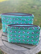 Two green patterned pouches on a wooden stool outdoors.