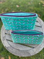 Two turquoise patterned zipper pouches on a wooden surface with grass background