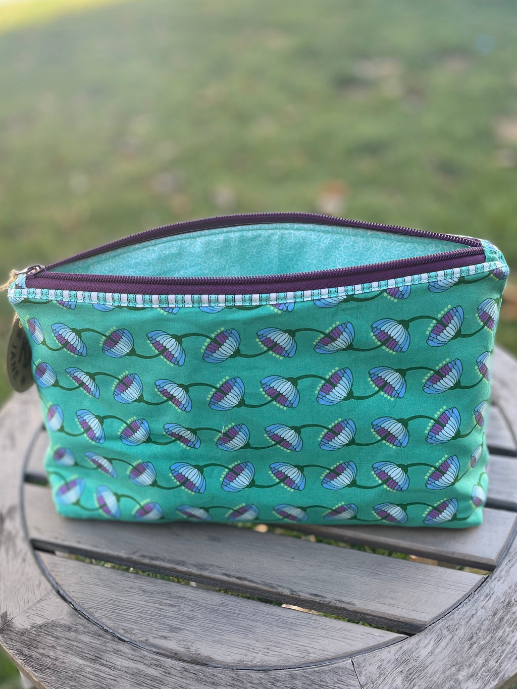 Green fabric pouch with blue pattern on a wooden stool outdoors