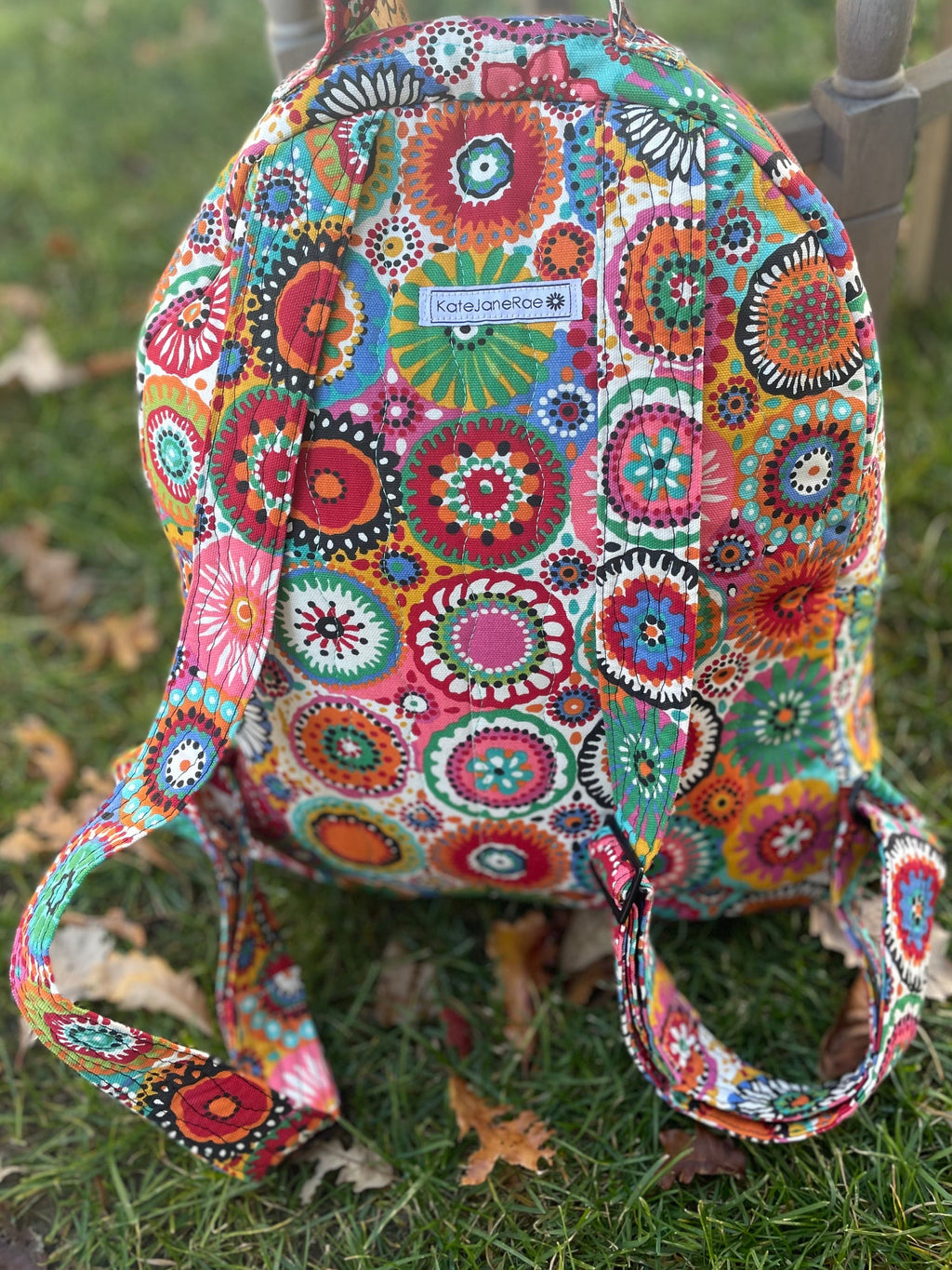 Colorful patterned backpack on grass with a chair in the background