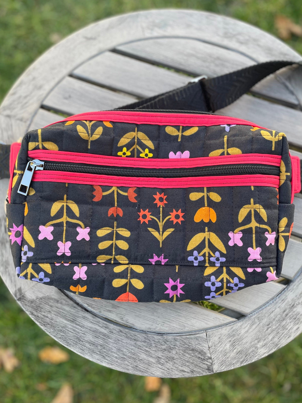 Fanny pack with floral pattern and pink zippers on a wooden chair outdoors.