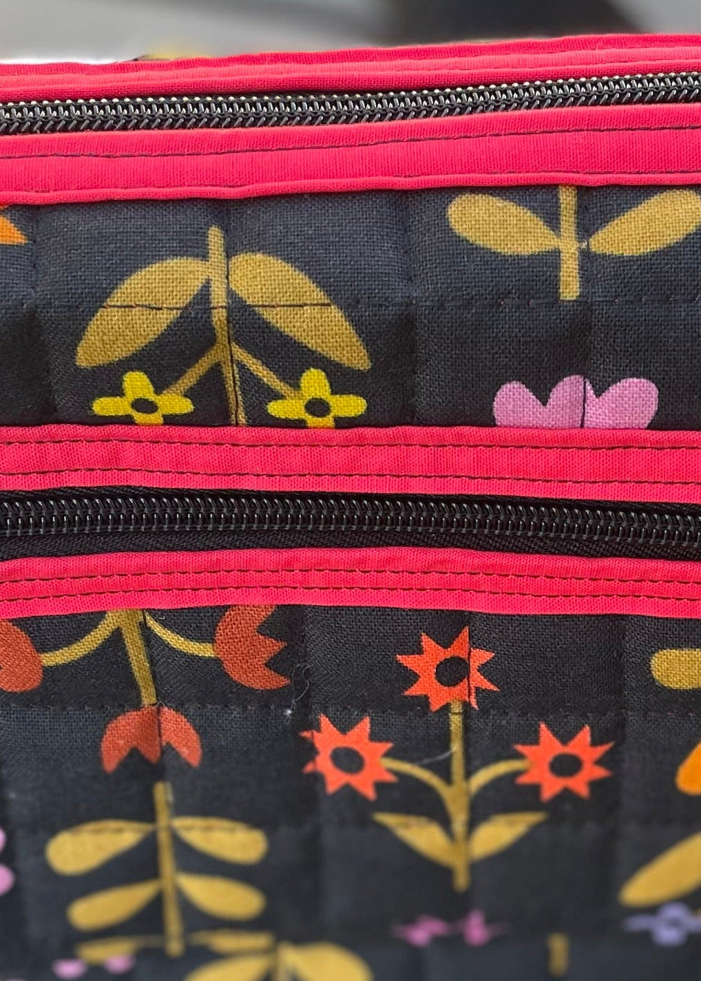 Floral-patterned pouch with red zipper on a stone surface with grass background