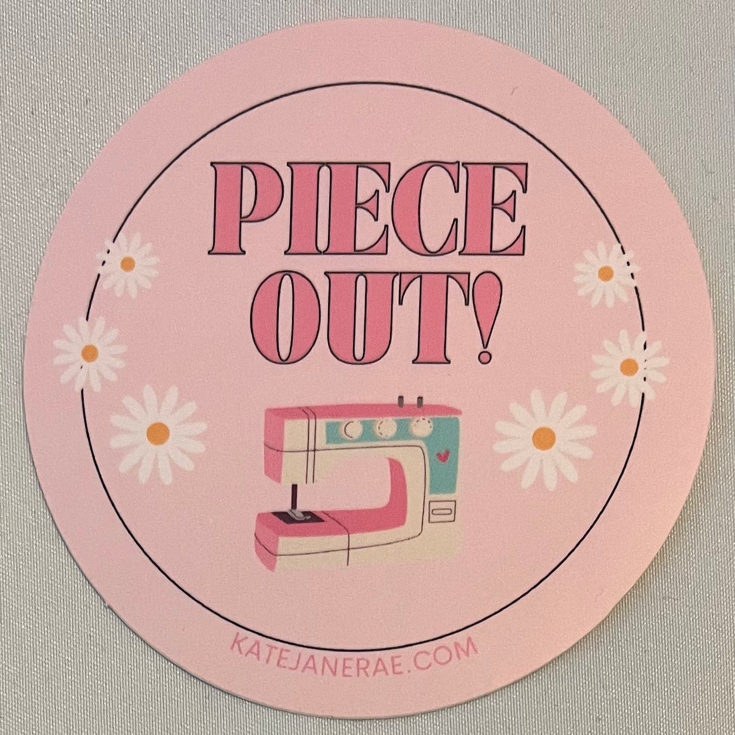 Round pink sticker with text and floral design on a textured surface