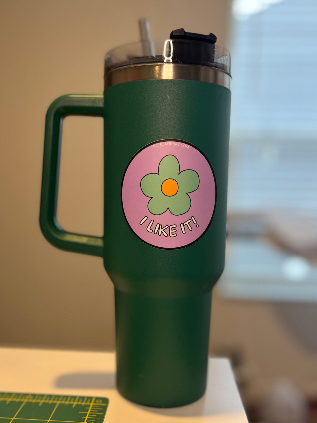 Green mug with a pink flower-shaped label on a surface