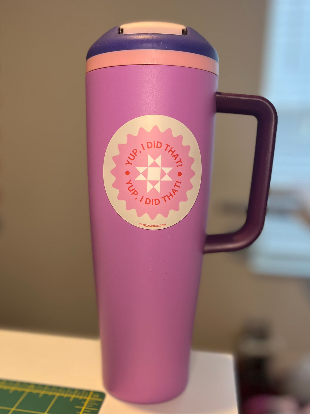 Purple tumbler with a handle and a circular sticker on a table.