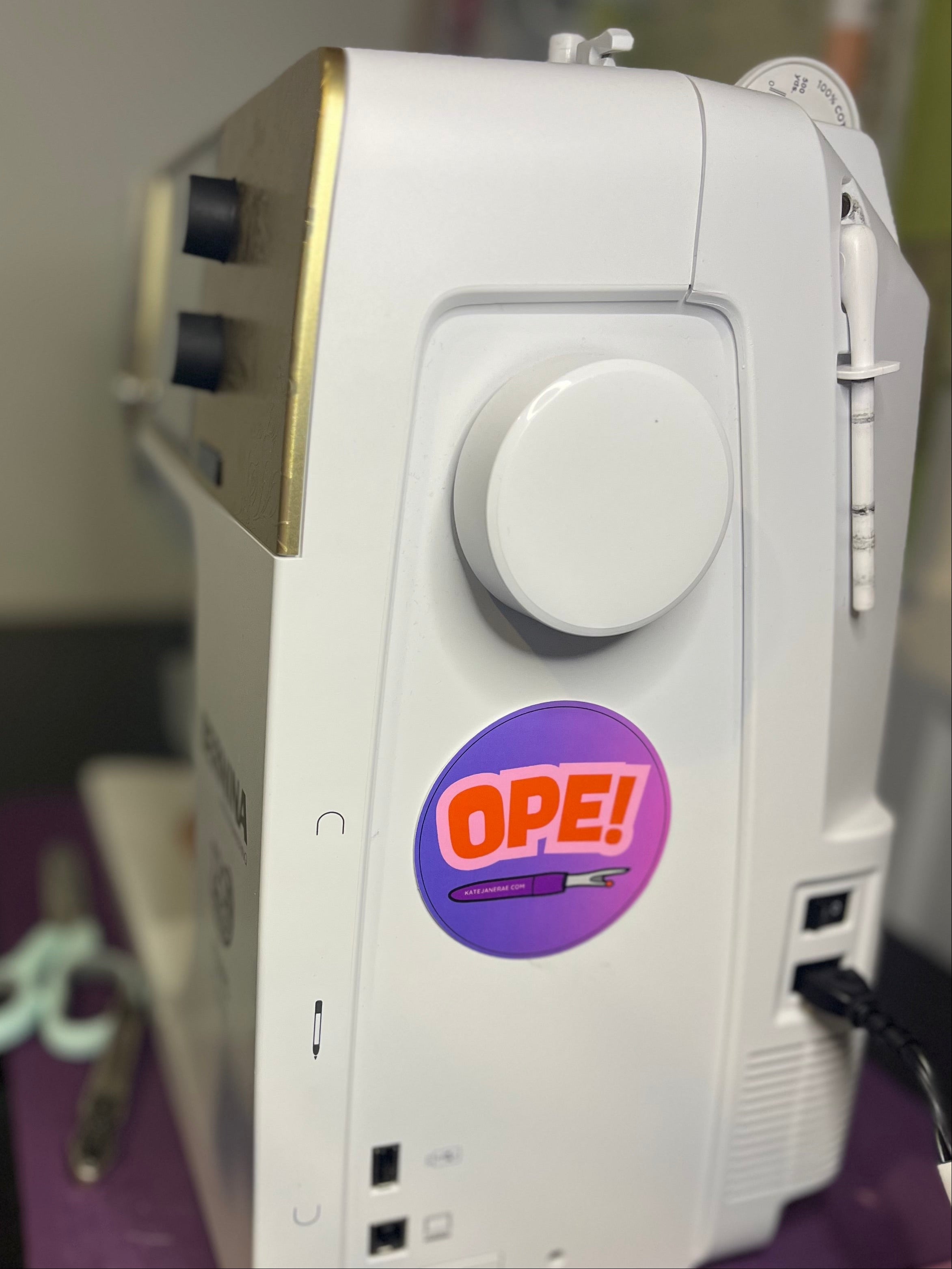 White sewing machine with a purple 'OPE!' sticker on a dark surface.