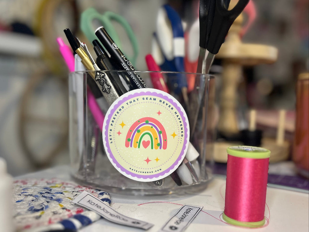 Clear holder with stationery items including pens and scissors, with a colorful rainbow sticker on a blurred background.