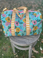 Floral-patterned duffel bag with striped handles on a chair outdoors.