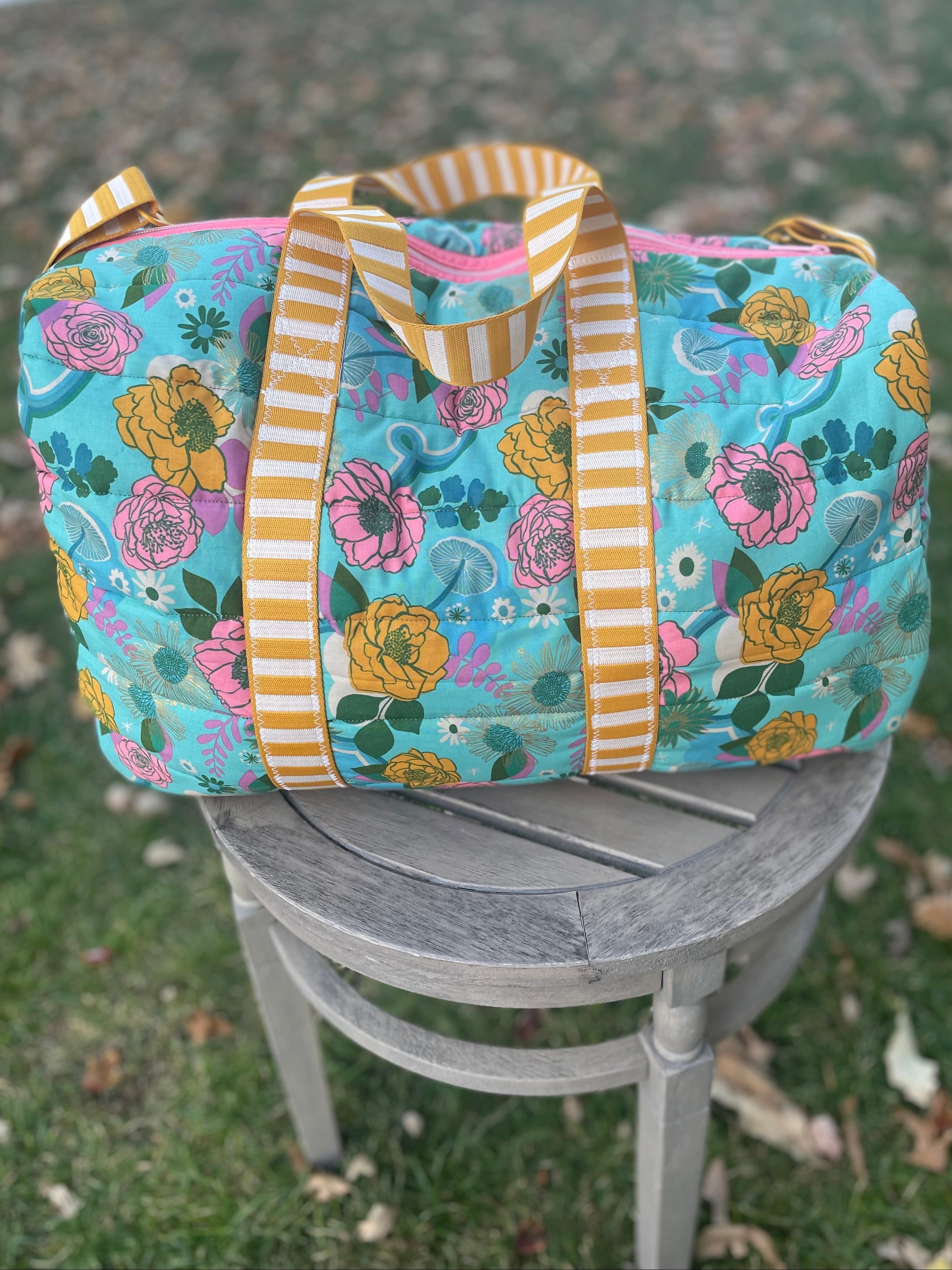 Floral-patterned duffel bag with striped handles on a chair outdoors.