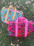 Two floral-patterned bags with colorful straps on a grassy background