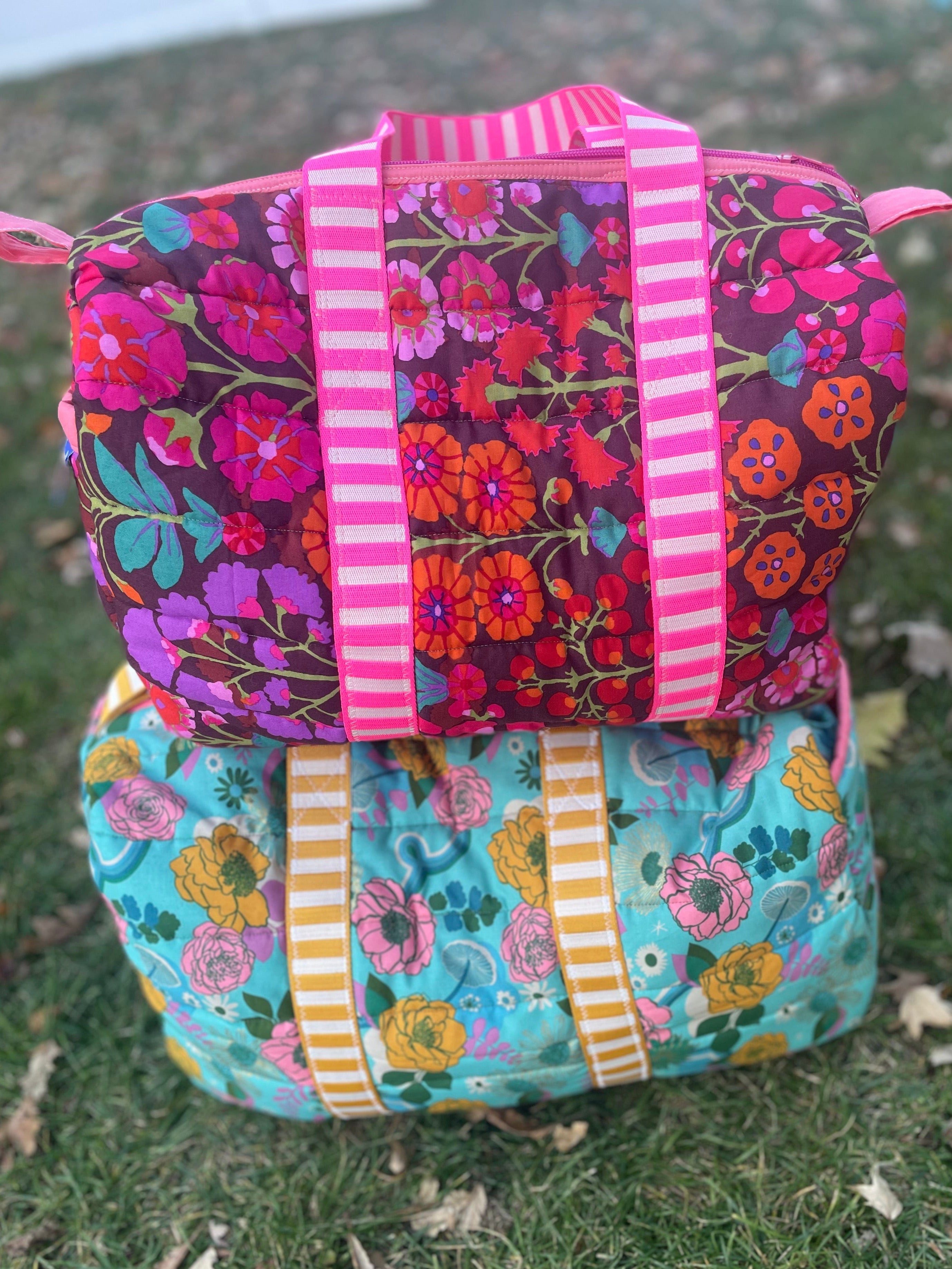 Two floral-patterned bags with colorful straps on a grassy surface