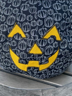 Black bag with white pumpkin pattern and yellow logo on a wooden surface