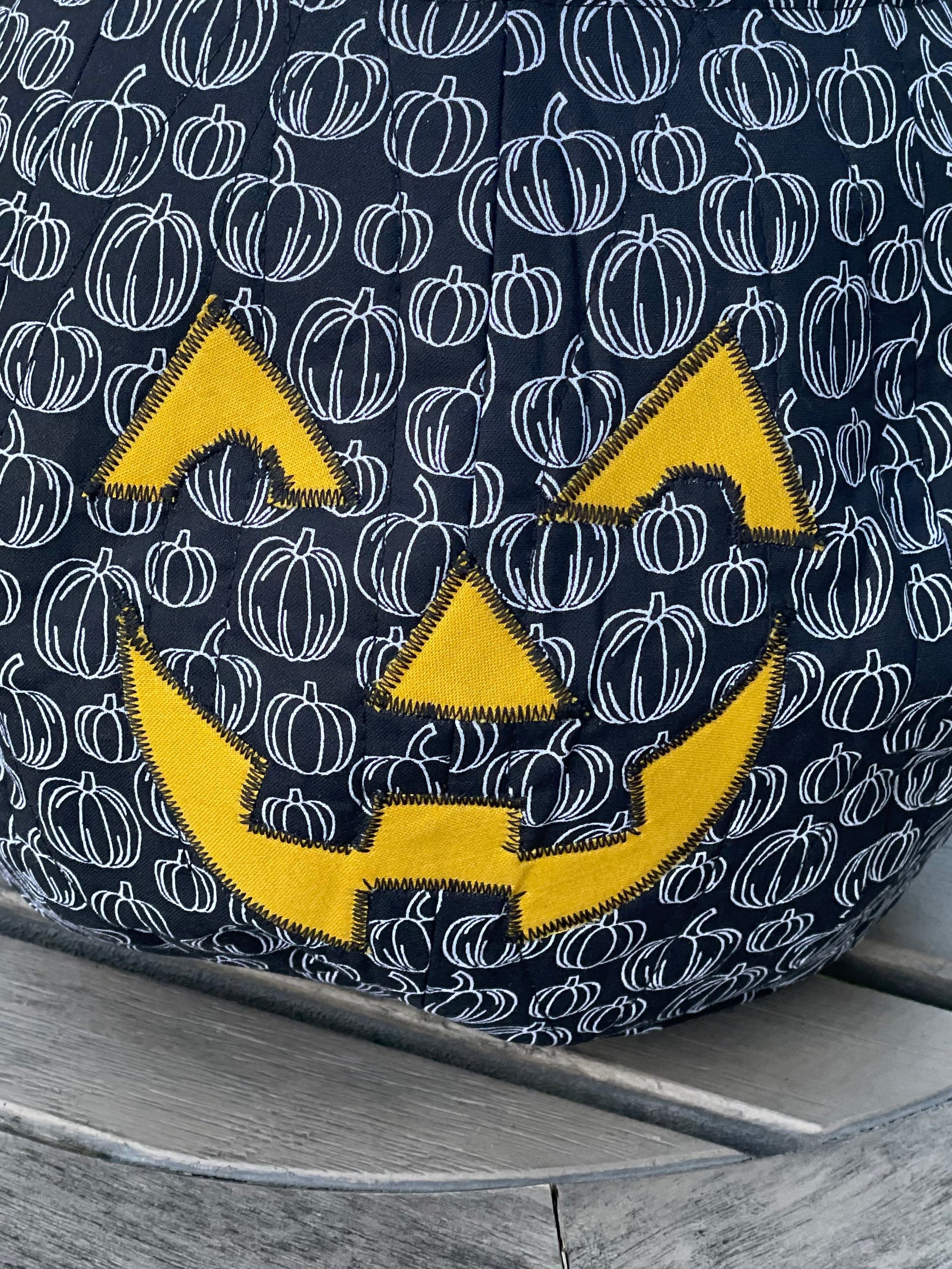 Black bag with white pumpkin pattern and yellow logo on a wooden surface