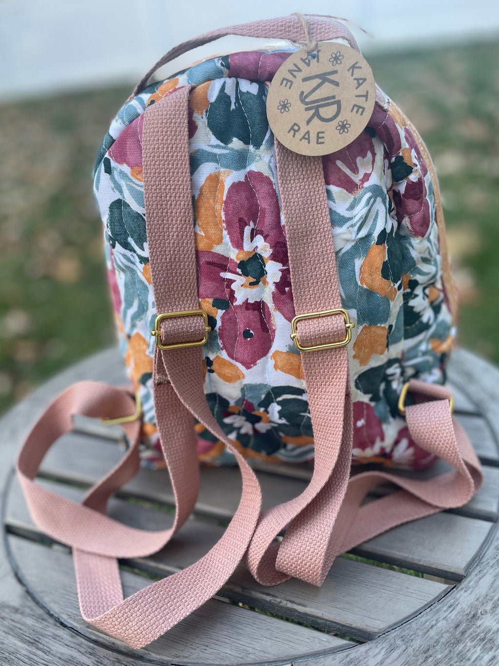 Floral-patterned backpack with pink straps on a wooden surface