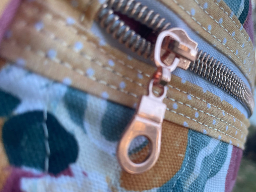 Close-up of a floral-patterned bag with a gold zipper pull.