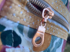 Close-up of a floral-patterned bag with a gold zipper pull.