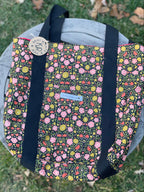 Floral-patterned bag with black straps on a grassy background