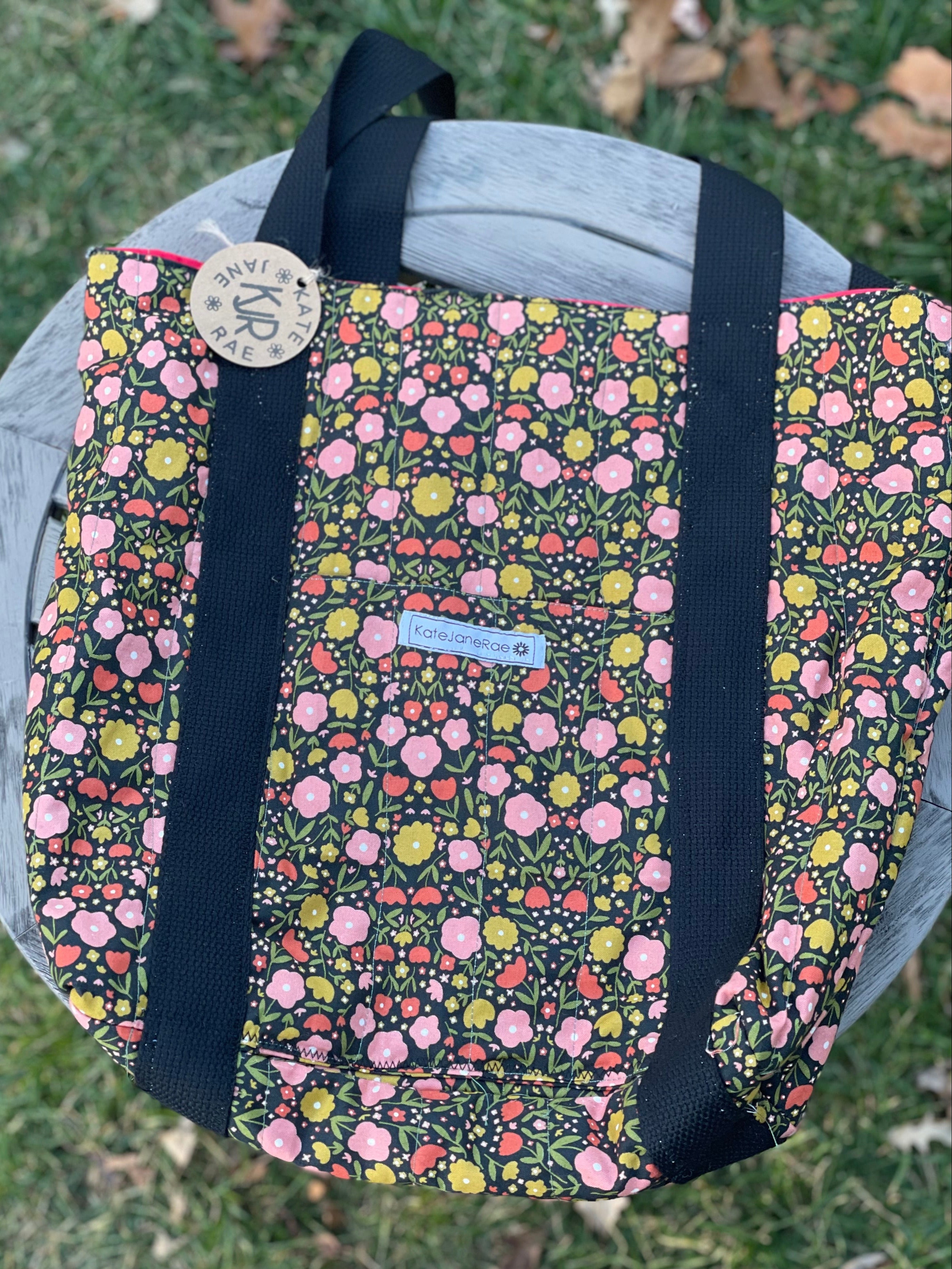 Floral-patterned bag with black straps on a grassy background