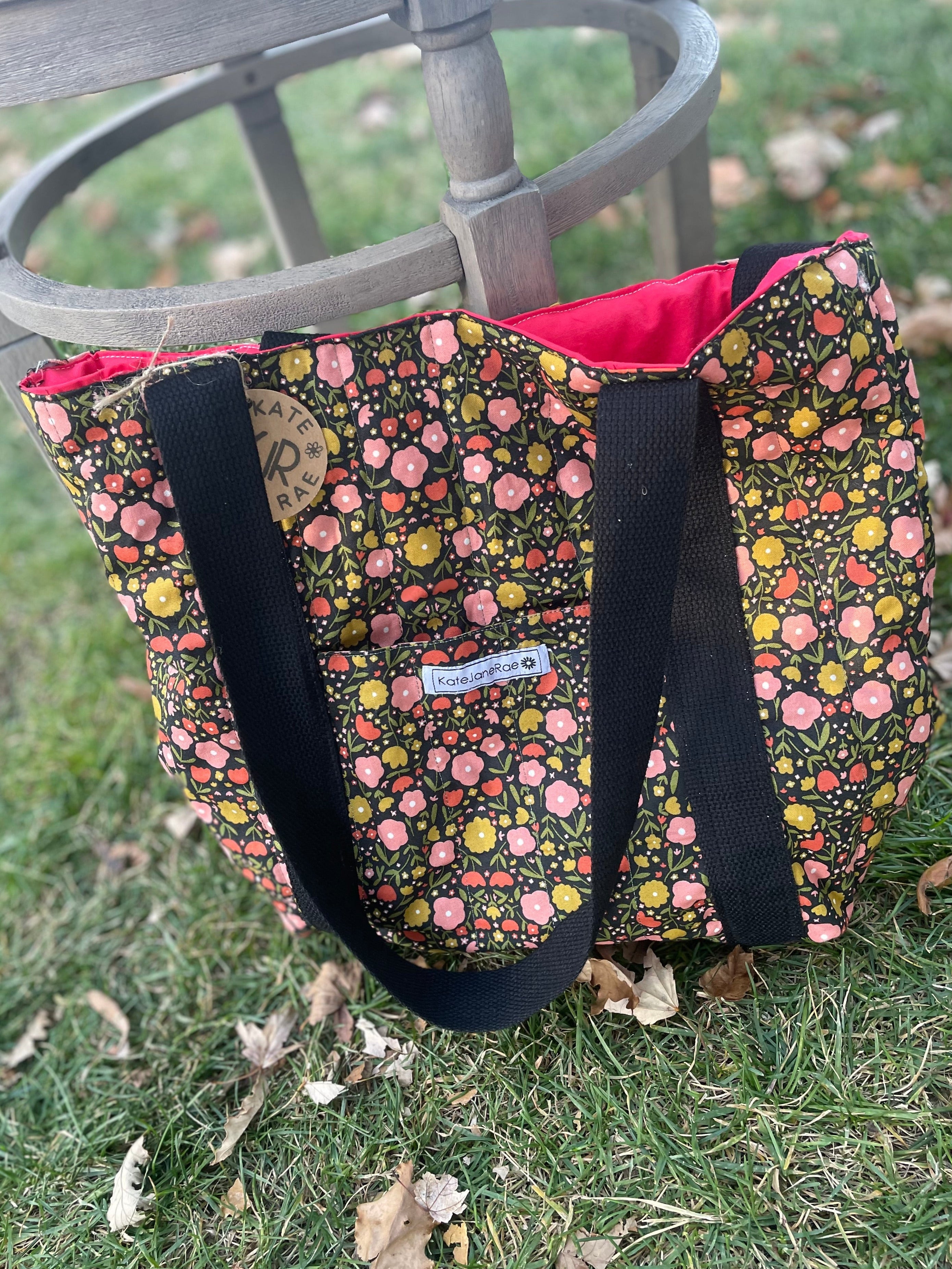 Floral-patterned bag with black straps on a grassy surface