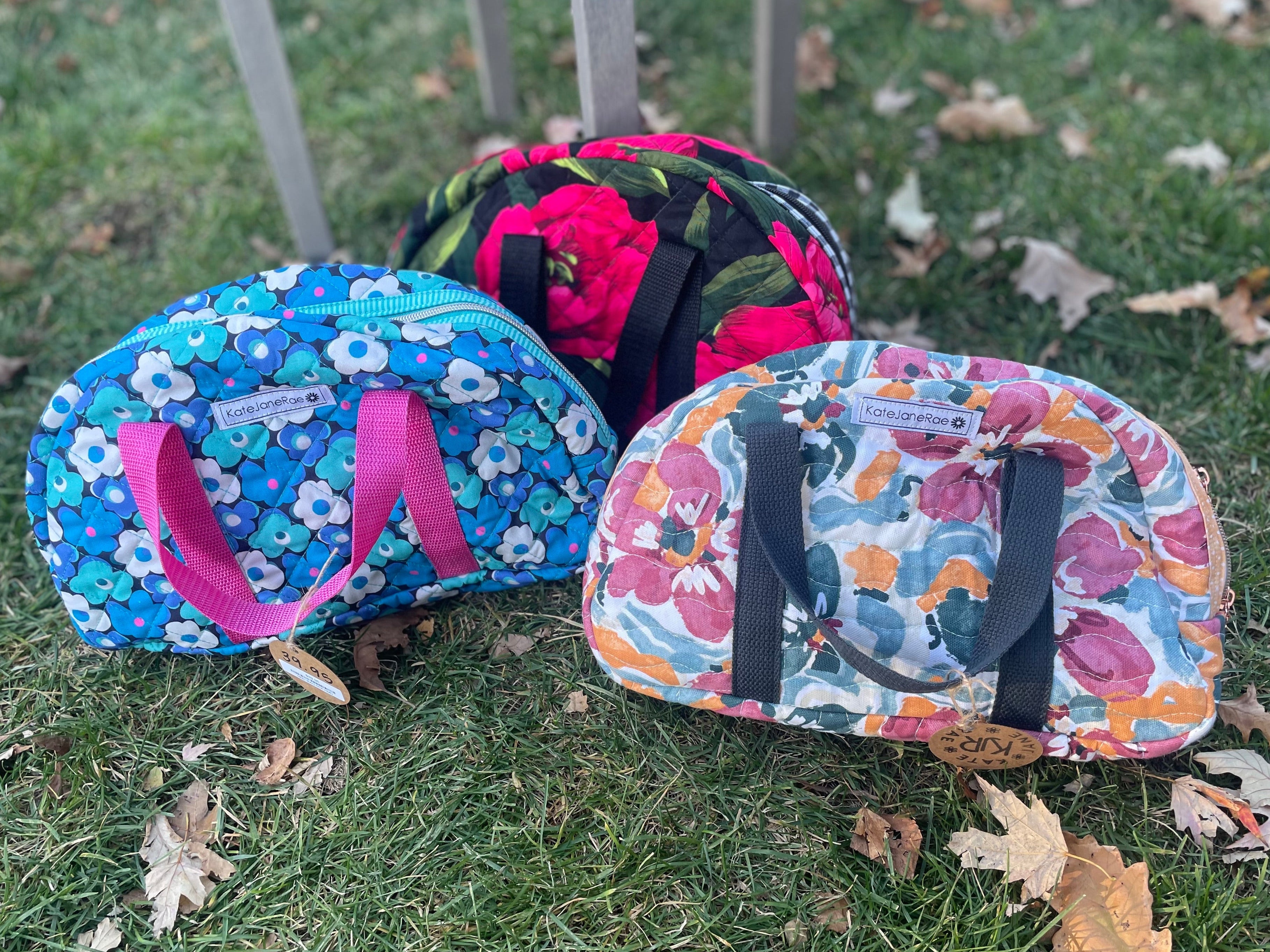 Three floral-patterned bags on a grassy surface with fallen leaves.