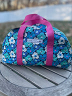 Blue floral-patterned bag with pink straps on a wooden surface outdoors