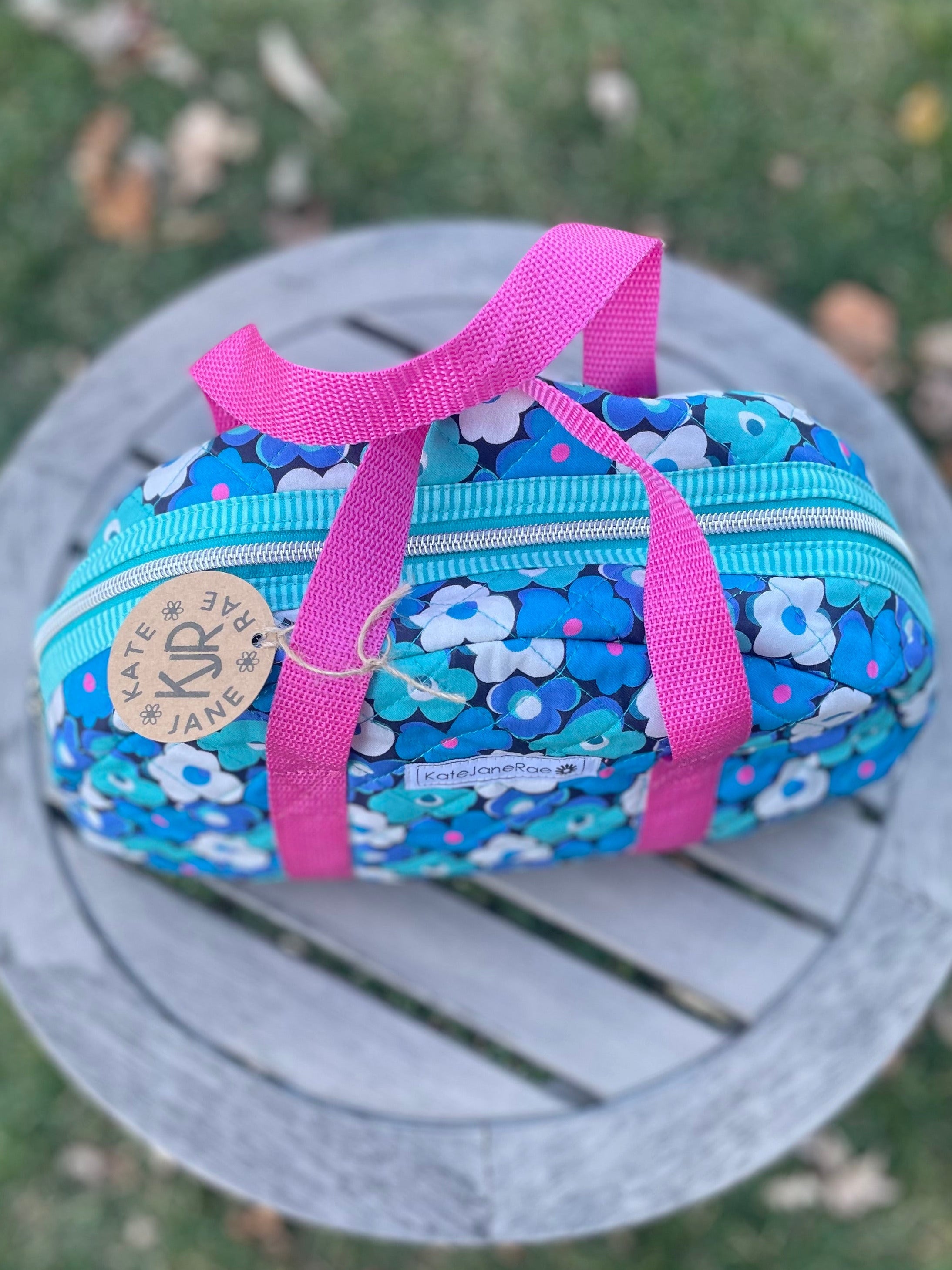 Blue floral pencil case with pink ribbons on a round stone surface outdoors.