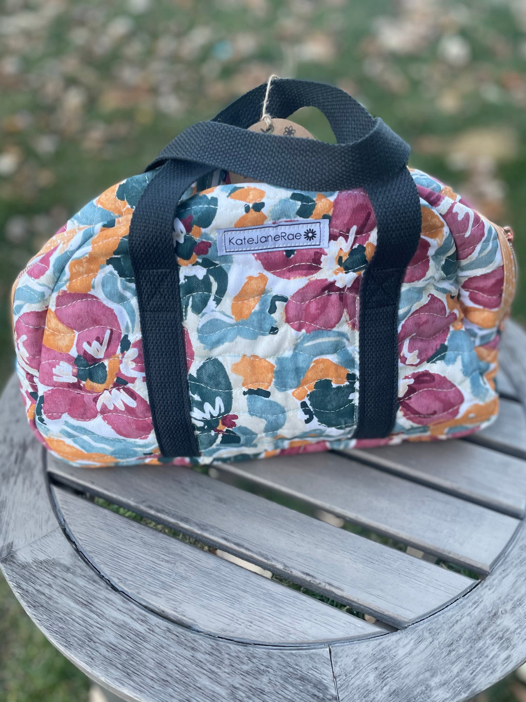 Floral-patterned bag with black straps on a wooden surface outdoors
