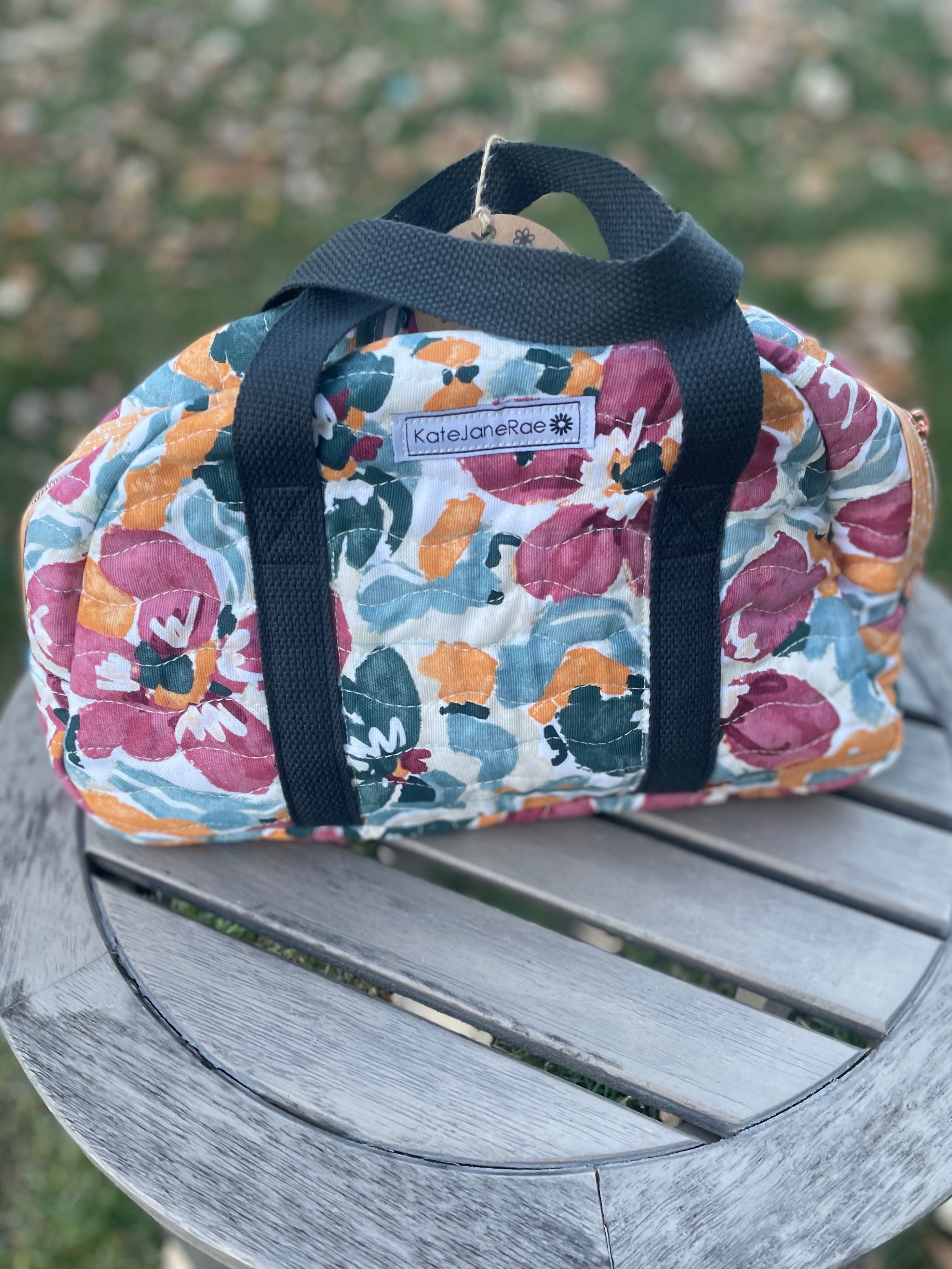 Floral-patterned bag with black straps on a wooden surface outdoors