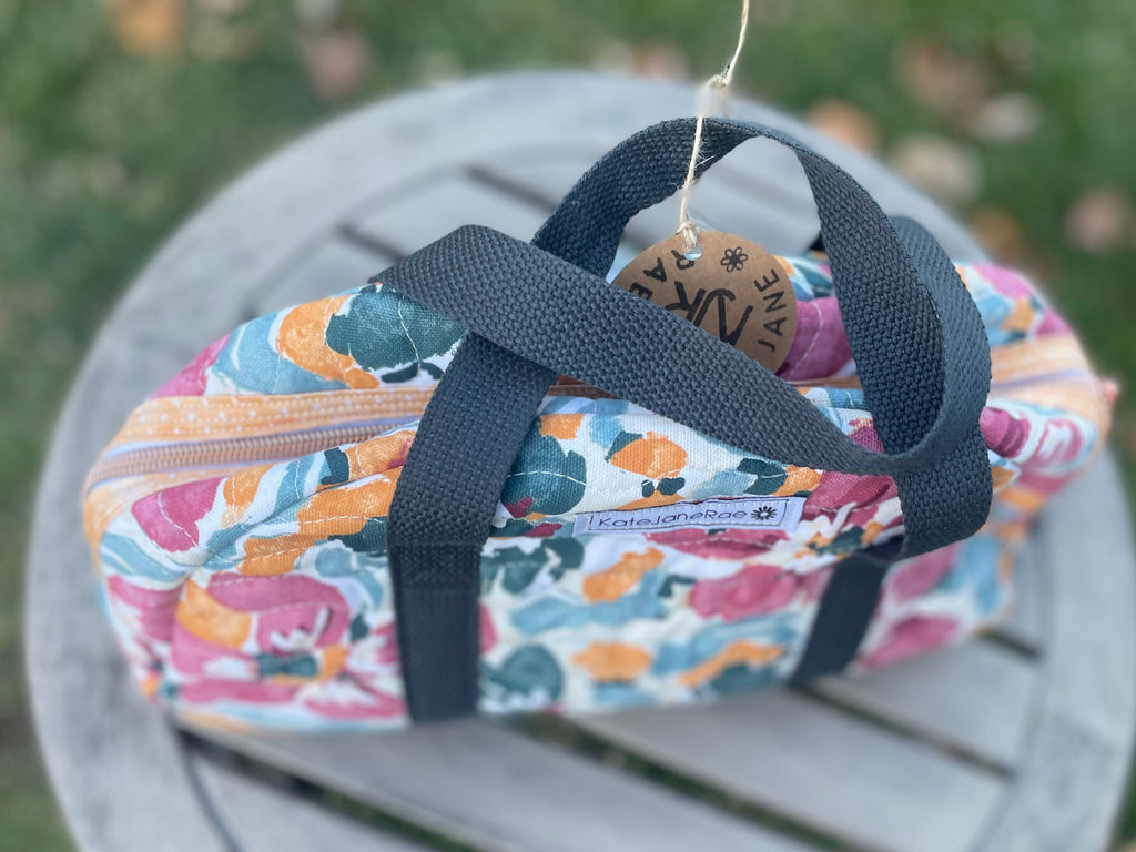 Colorful floral-patterned bag with a black strap on a wooden surface.