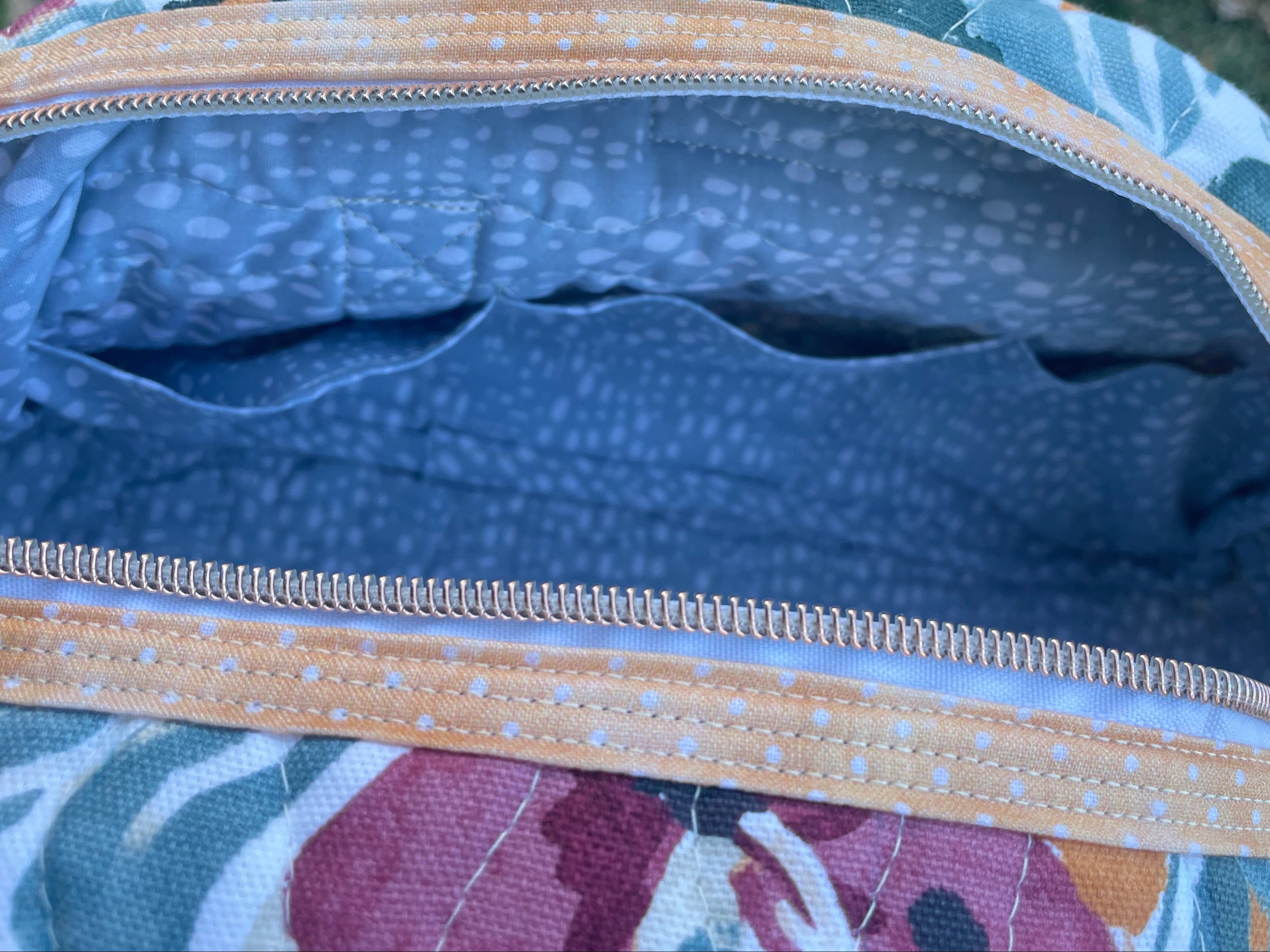 Floral-patterned bag with a zipper on a grassy background