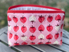 Pink pouch with strawberry pattern on a wooden surface