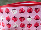 Pink pouch with strawberry pattern on a wooden surface