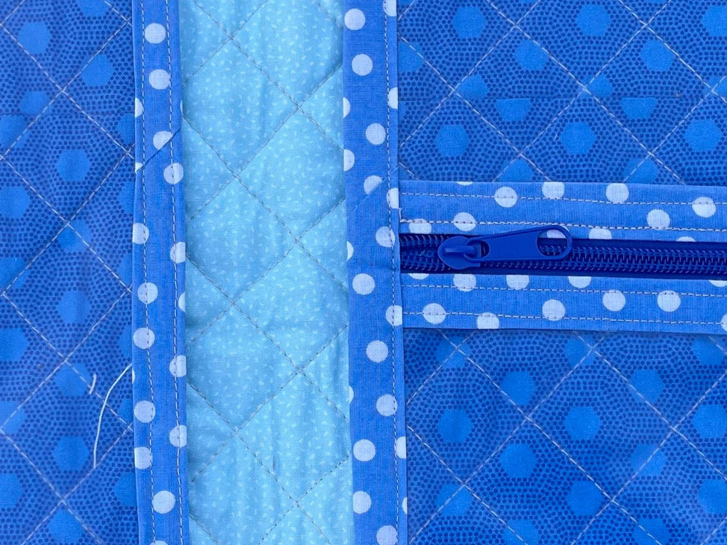 Blue quilted bag with white polka dots on a grassy background