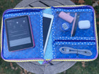 Blue quilted pouch with electronic items on a grassy surface