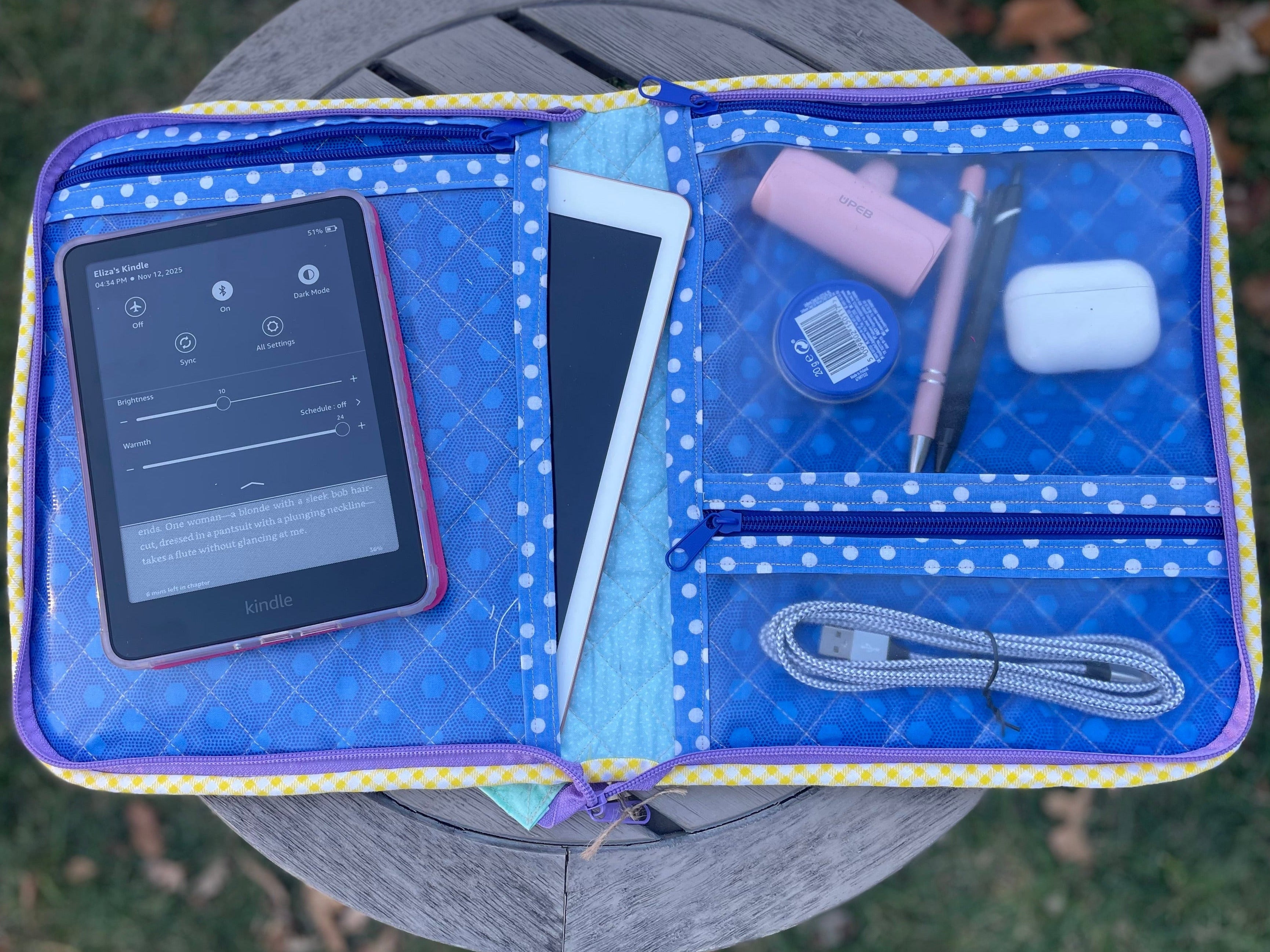 Blue quilted pouch with electronic items on a grassy surface