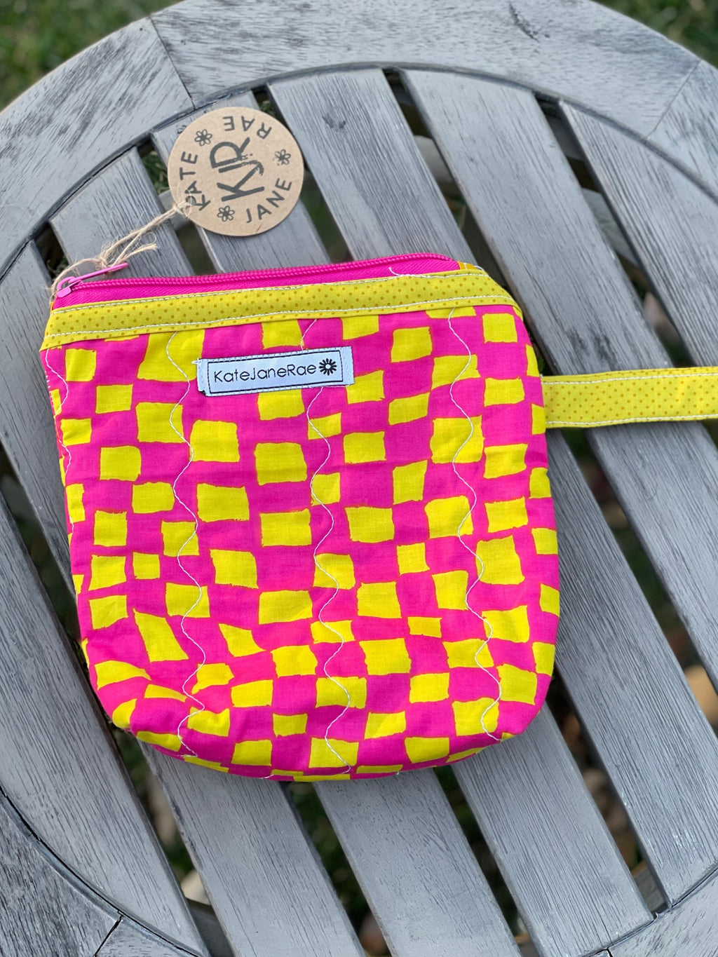 Pink and yellow checkered pouch on a wooden surface with a brand label.