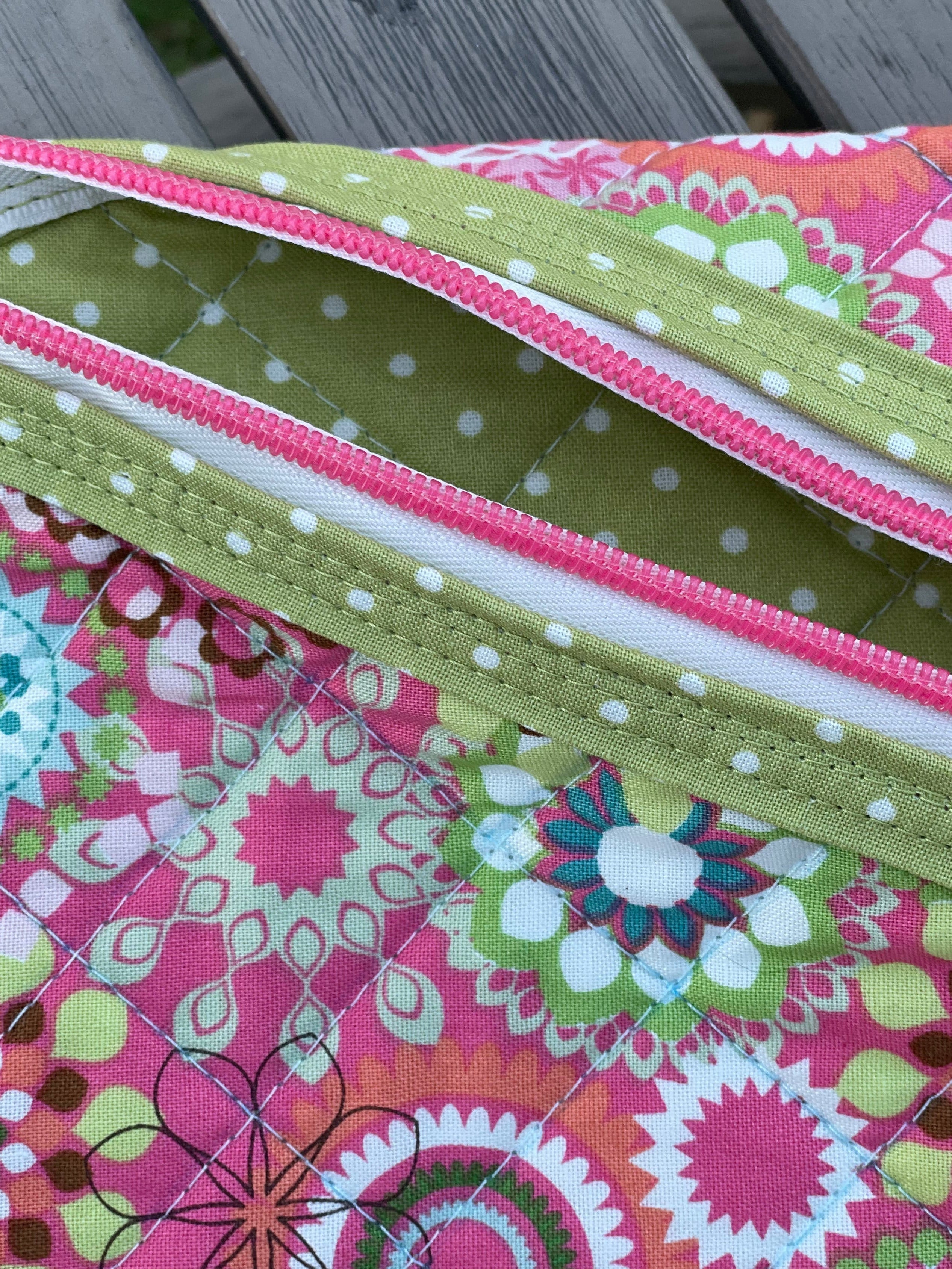 Close-up of a colorful quilt with pink and green patterns on a wooden surface.