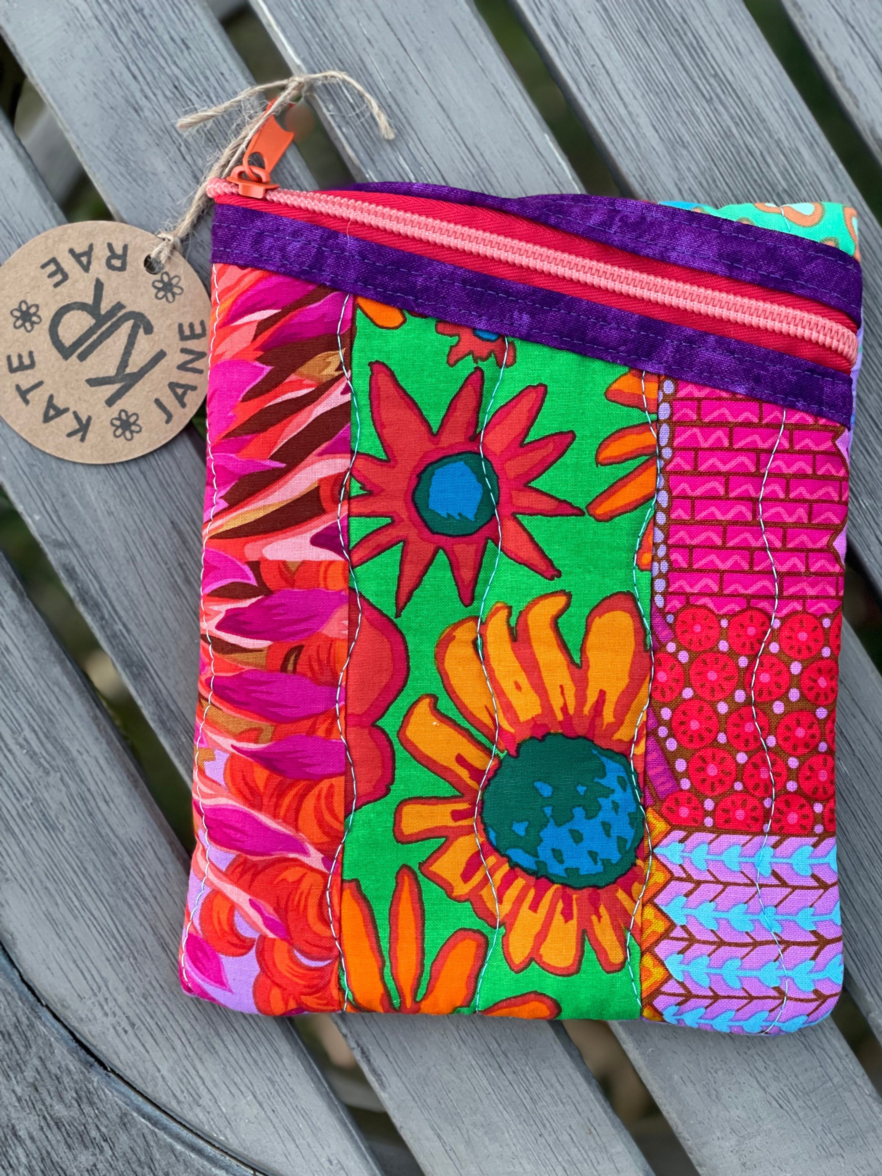 Colorful floral fabric pouch on a wooden surface with a brand tag.