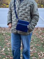 Person wearing a quilted jacket and blue jeans standing on grass with a white door in the background
