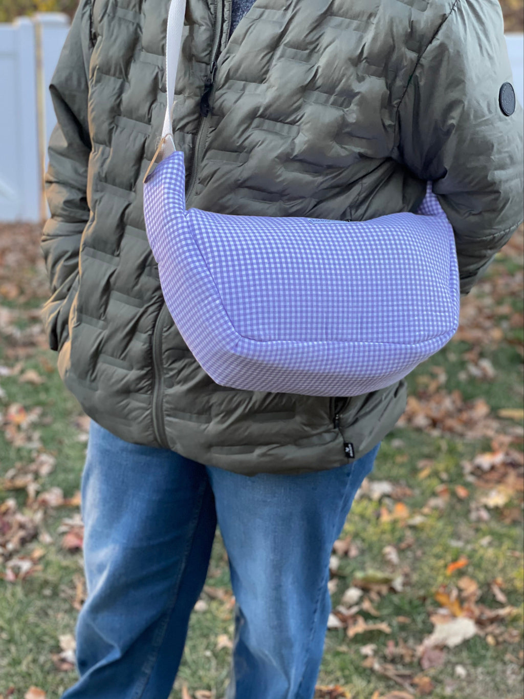 Person wearing a green puffer jacket with a purple mesh bag over their shoulder outdoors.
