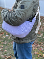 Person wearing a green jacket holding a purple checkered bag outdoors on a grassy area.
