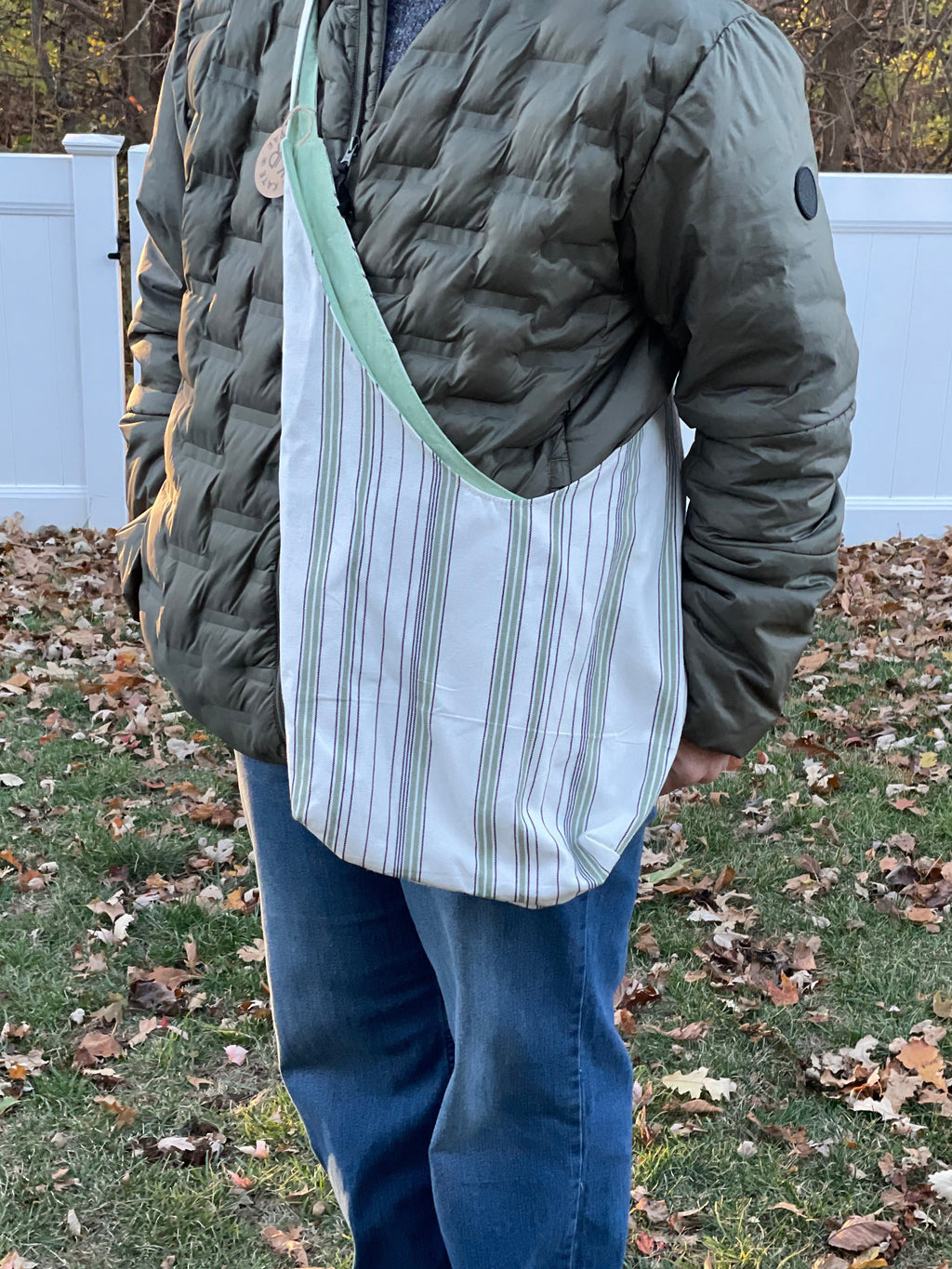 Person wearing a green jacket and blue jeans standing on grass with fallen leaves.