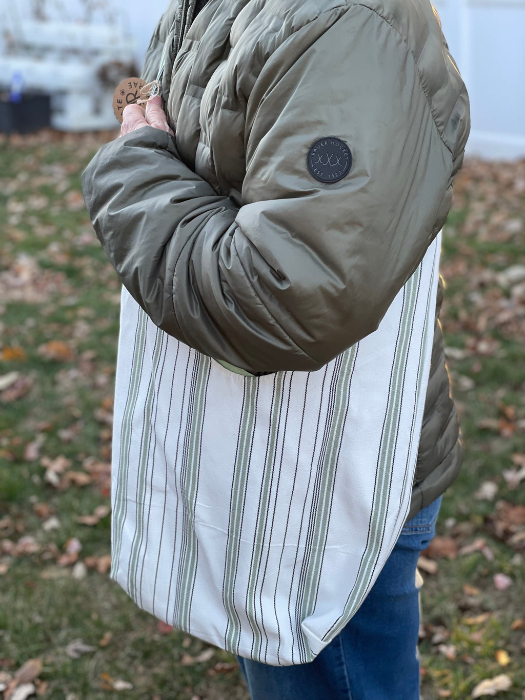 Person wearing a green puffer jacket with a white striped shirt and blue jeans outdoors.