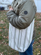 Person wearing a green puffer jacket with a white striped shirt and blue jeans outdoors.