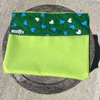Green fabric and jelly vinyl zipper pouch on wooden table.