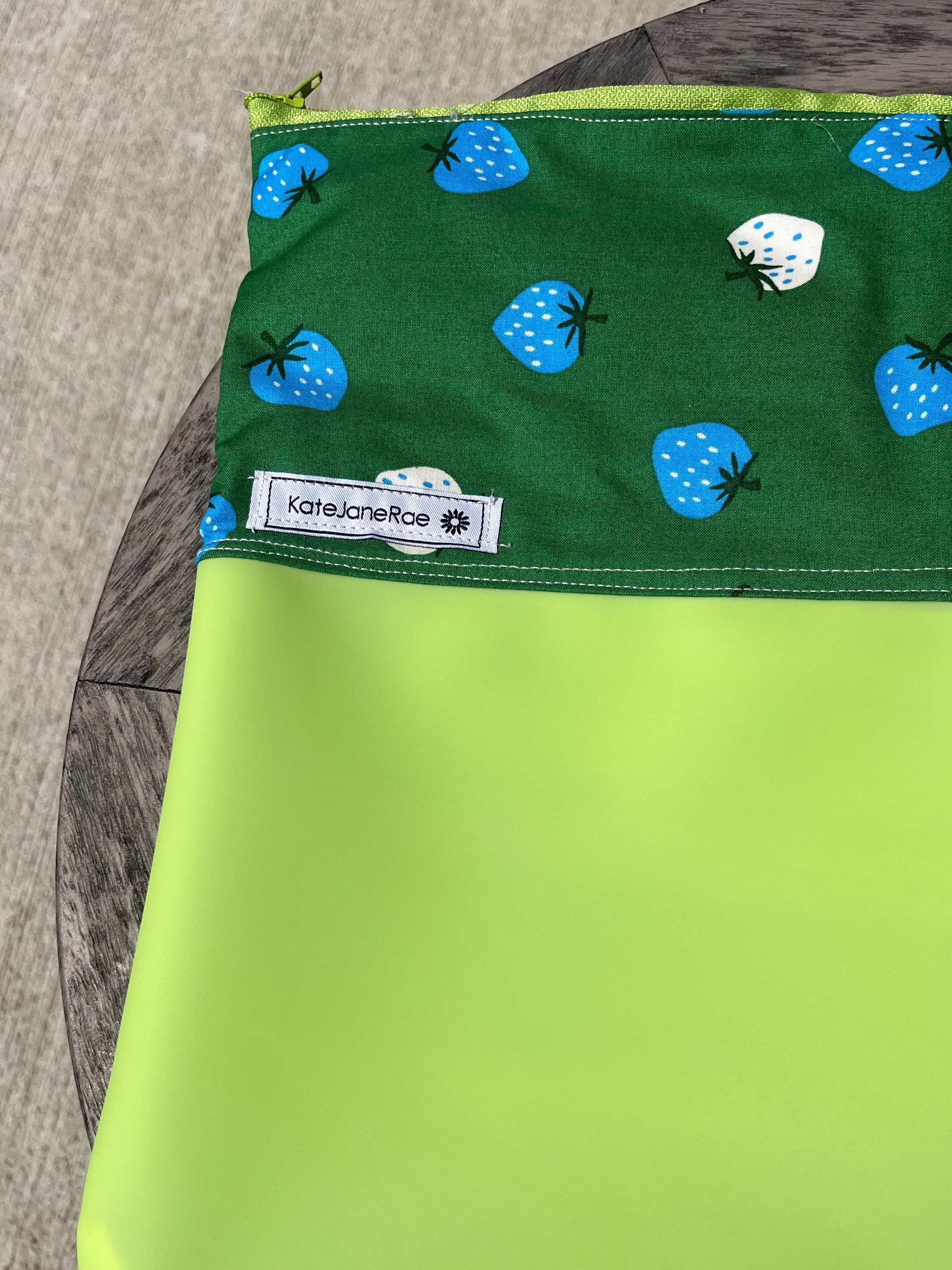 Green fabric and jelly vinyl zipper pouch on wooden table.