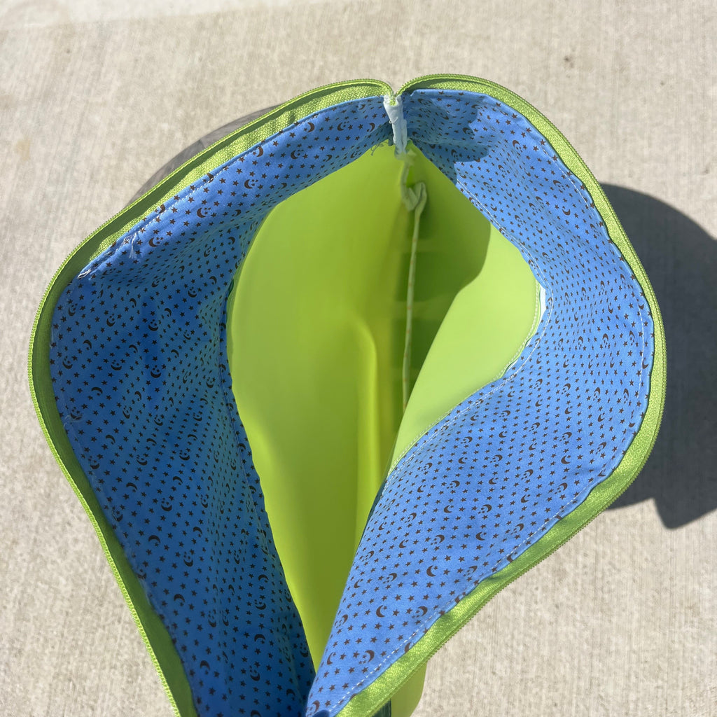 Green fabric and jelly vinyl zipper pouch on concrete surface.
