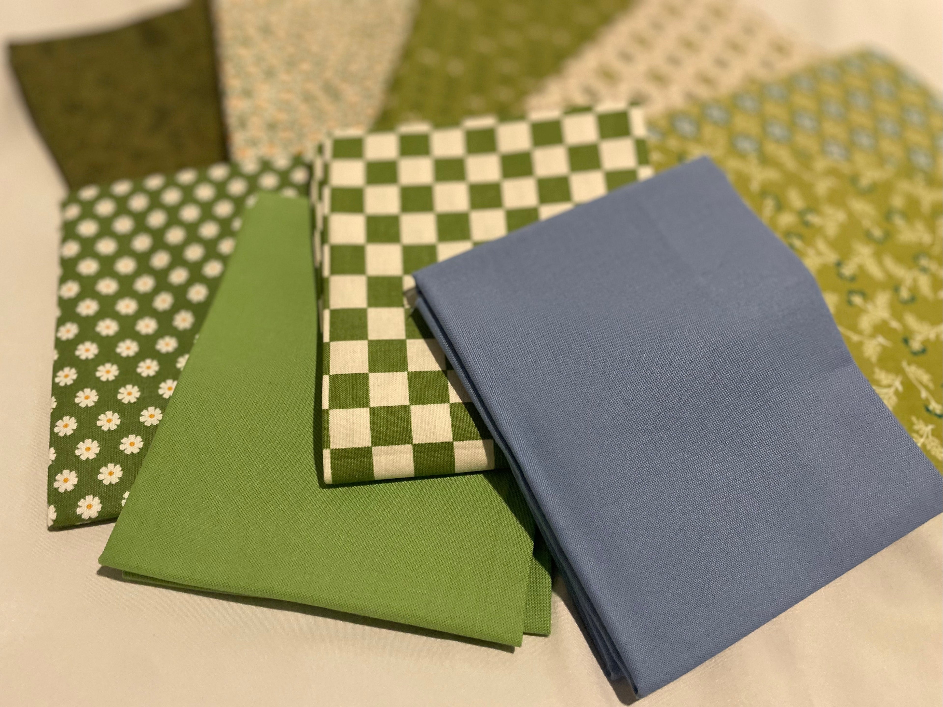 Collection of green and blue fabric swatches on a beige surface