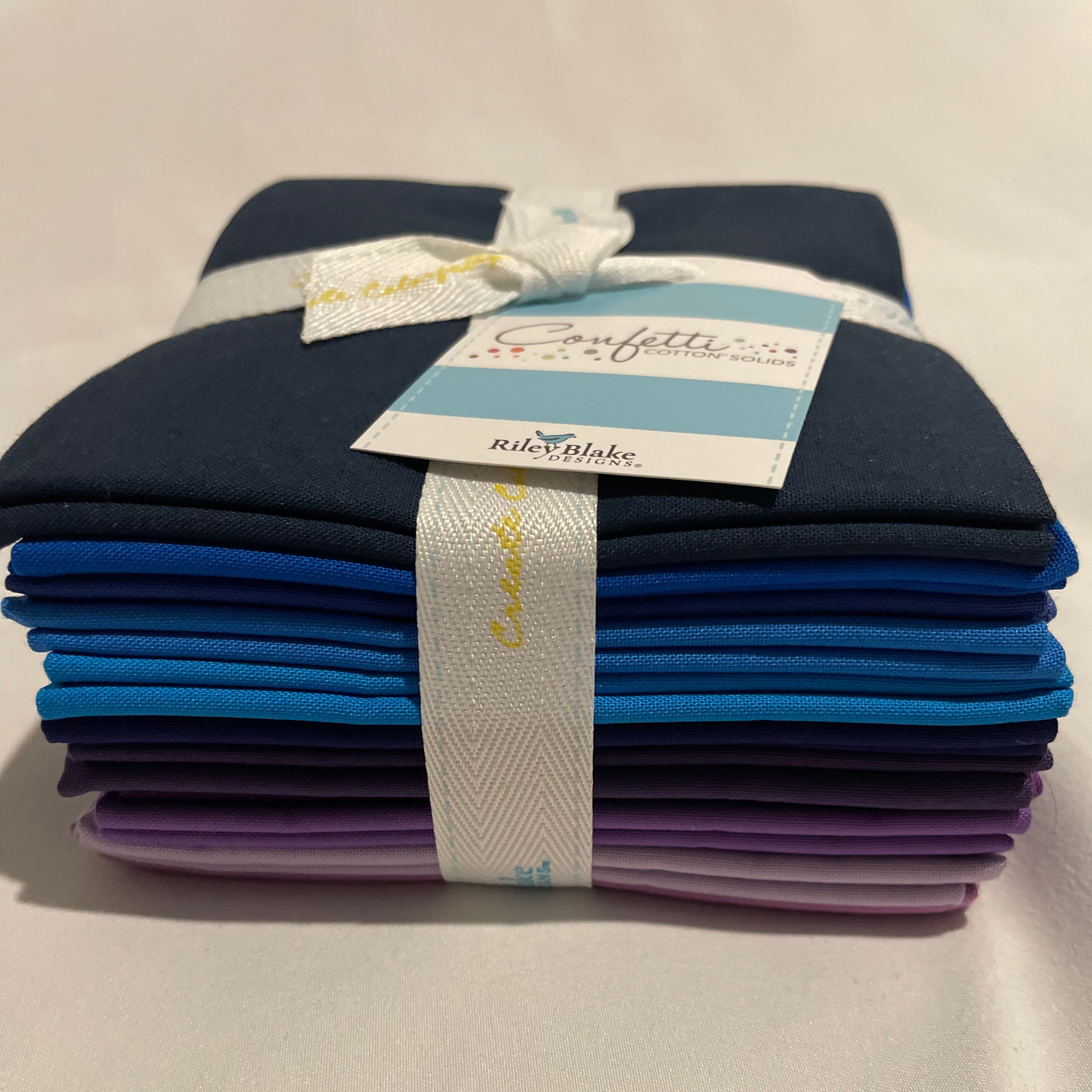 Set of folded fabric swatches in blue and purple with a label on a beige background
