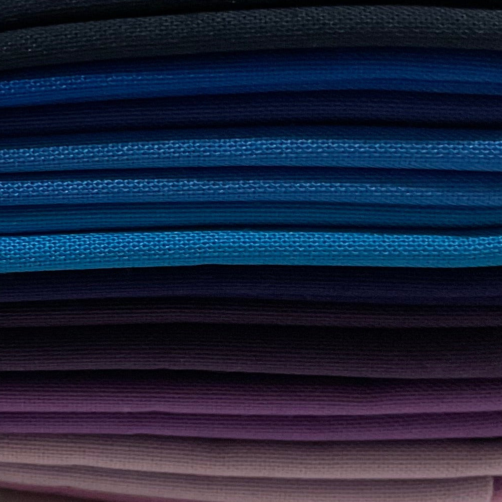 Set of folded fabric swatches in blue, purple, and navy with a label on a beige background